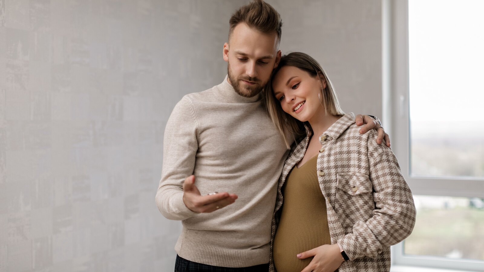 A partner holding a pregnant woman close by a window